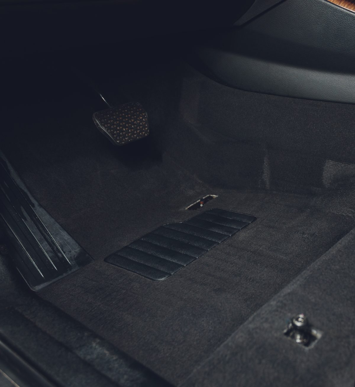 Dark car interior floor mats with ventilation grille and branded emblem visible