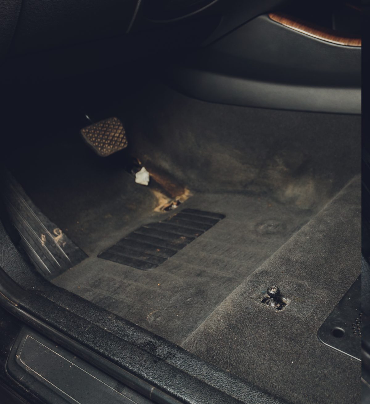 Car interior floor mats with worn fabric and metal fasteners visible in dim lighting